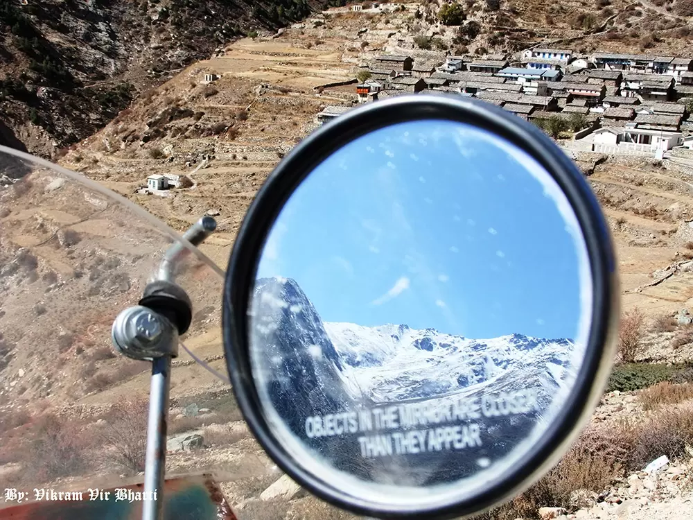 A beautiful view of Niti Village, Chomoli in the background and snow covered Himalayan view on the mirror of bike. This photo is taken to give a social message to the people to save mountain environment.. Pic: Vikram Vir Bharti 