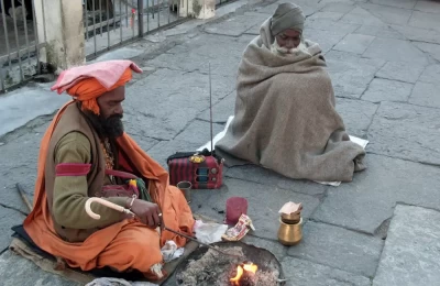 Two saints seated at religiously sacred Kedarnath temple yard trying to keep them warm in severe cold of November month. Noticeably, a radio might be the matter of time pass or entertainment to their simple living.